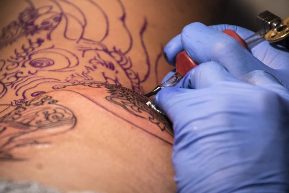 Tätowierer mit Handschuhen sticht ein Tattoo