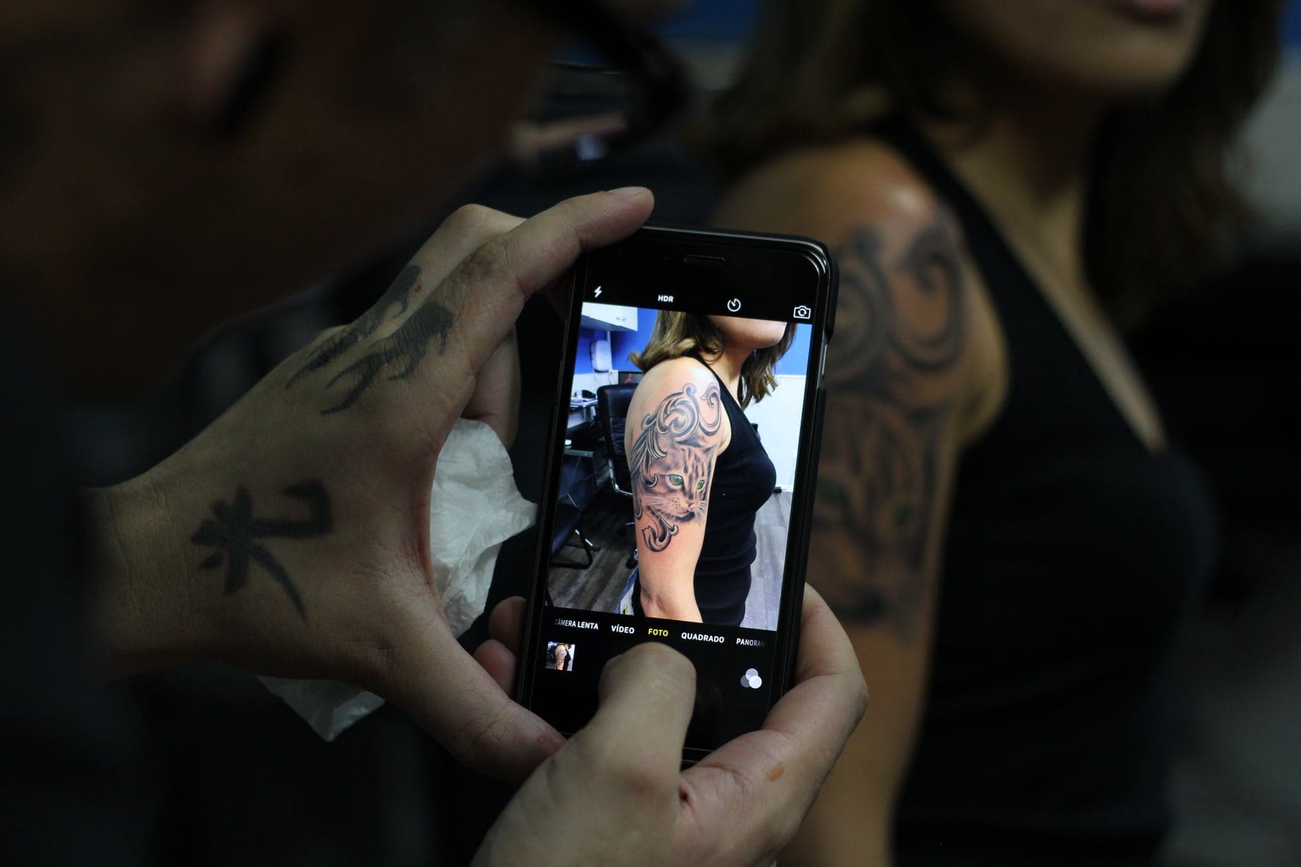 Tätowierte Hände fotografieren ein Arm-Tattoo mit dem Smartphone