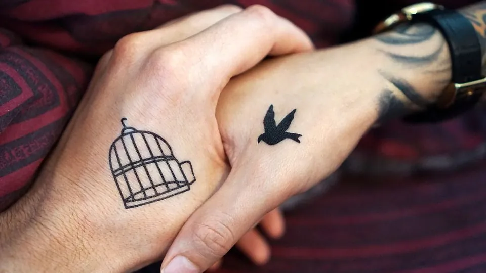 Zwei Hände mit Partner-Tattoos, Vogel und offener Käfig